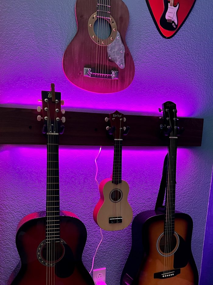 The same guitar rack at night, lit from behind by purple LED strip lighting.